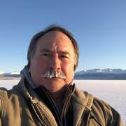 A man in a brown winter coat stands in a snowy landscape.