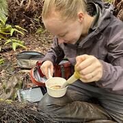 Person sitting on ground in rain gear holding a sample in a plastic cup and a baster.