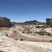 Dry desert landscape with rocky cliffs and sparse vegetation under a clear blue sky.