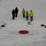 USGS scientists standing in the snow in front of an orange circular landing mat for their drone