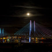 green, blue, purple and pink lighting on the bridge during a moonlit night