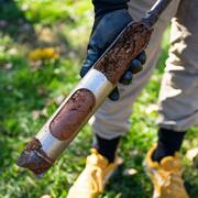 A scientist holds a cored sediment sample in a park.