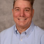 scientist smiling, with short blond/red hair, wearing a blue shirt