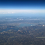 A photo taken from an airplane of a large, elongated lake surrounded by long mountain ridges and vineyards
