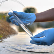 Pair of hands holding sample of water from river in glass test tube 
