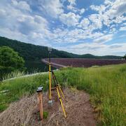 blue sky above curved aggregate dam with water surface, trees, and grass