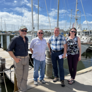 men and women standing on a dock on a sunny day near boats