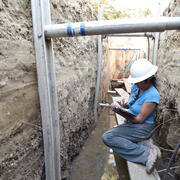 USGS scientist taking notes while seated on scaffolding inside a deep paleoseismic trench cut into the San Andreas fault.