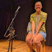 person sitting on stool next to microphone smiling