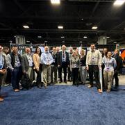 17 people stand in a row at a conference, smiling for the camera