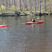 A woman kayaks upstream while towing an orange ADCP behind the kayak. 