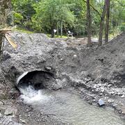 Clogged culvert pipe filled with sediment and some water running out of it.