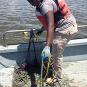 women with dark hair and orange vest pulling an oyster dredge on a boat