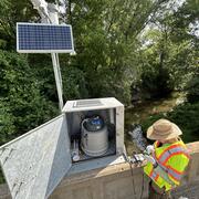 Scientist collecting field parameters and checking the autosampler at streamgage on bridge