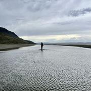 person in shilouette walking away from the camera in the shallows along a shoreline