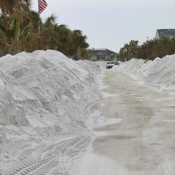 Sand that overwashed a coastal road is piled high on both sides of a road after preliminary clearing.