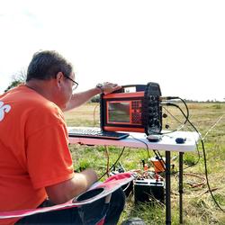 man in fields in chair reading data from instrument on table