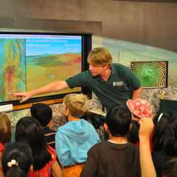 Scientist pointing to graphic on a screen while children watch