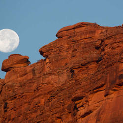 Full moon appearing over red rocks in Grand Canyon.