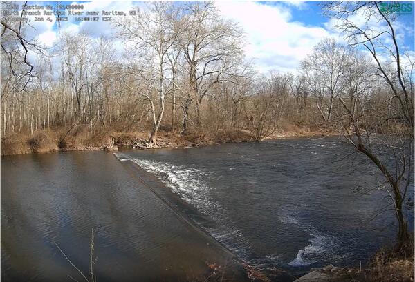 Looking down upon a weir creating a small drop and turbulence in a river with bare winter trees on the far bank