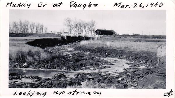 An image of Muddy Creek at Vaughn, Montana. Water level is low and mud covers banks. 
