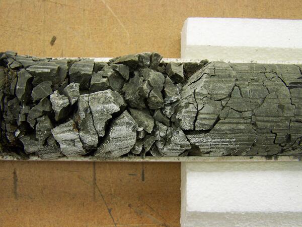 Dark, crumbly rock in a core tube