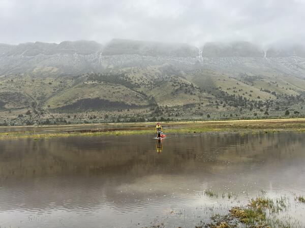 A female in safety gear pulling equipment through the water looking small amidst the stunning background of misty hills