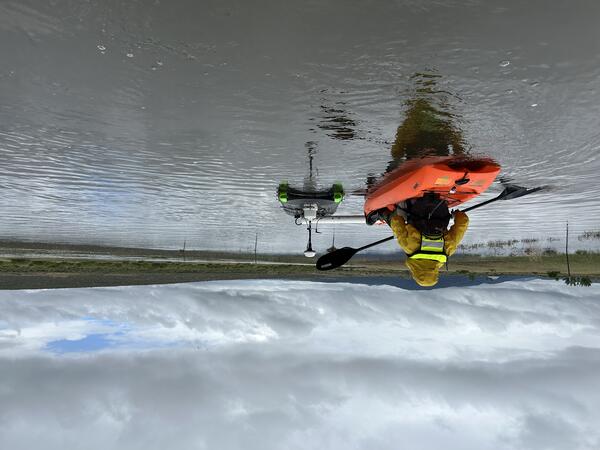 back view of a kayaker paddling to push measurement equipment pontoon across calm waters on a cloudy day