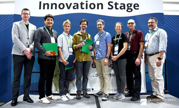 Eight people standing shoulder to shoulder in front of a banner reading Innovation Stage.