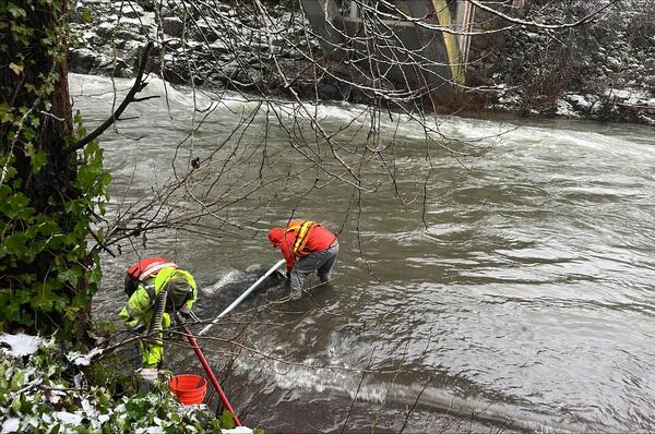 men in safety gear stand in rushing water fixing a pipe to the river bank