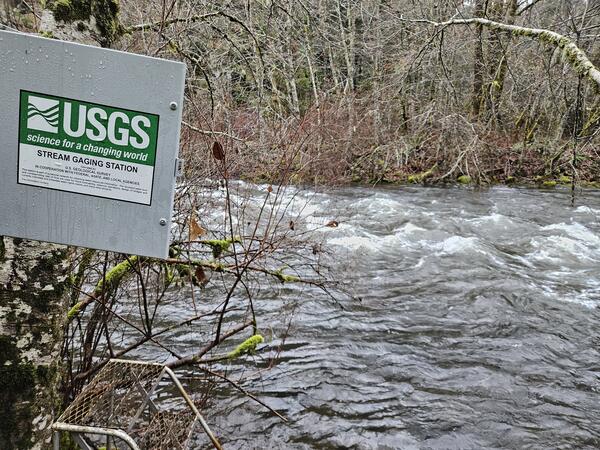 square metal enclosure door with USGS signage swings open by a rushing river