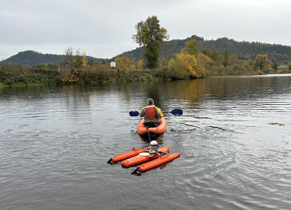 man paddles orange kayak towing an orange boat with flow measurement equipment 