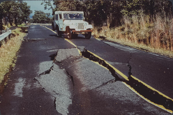 Color photograph of road cracks with vehicle in the background