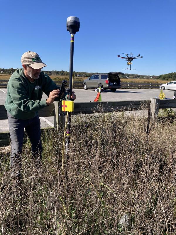 person using equipment in vegetation next to parking lot