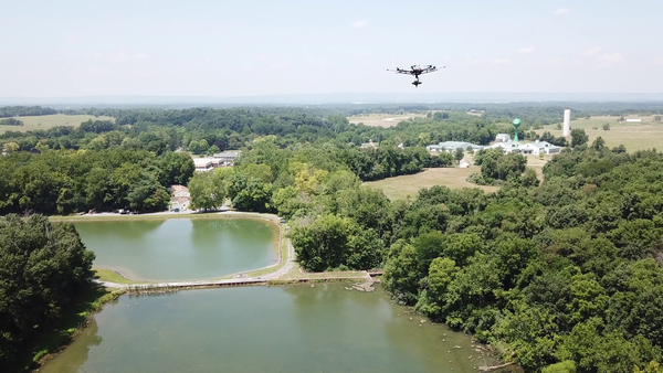 drone flying above reservoir located in a tree-covered landscape