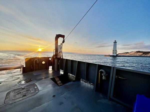 A sunset and a lighthouse pictured from the deck of a research vessel