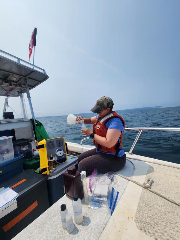 Researcher sitting on a small vessel pouring lake water in bottles for nutrient analysis