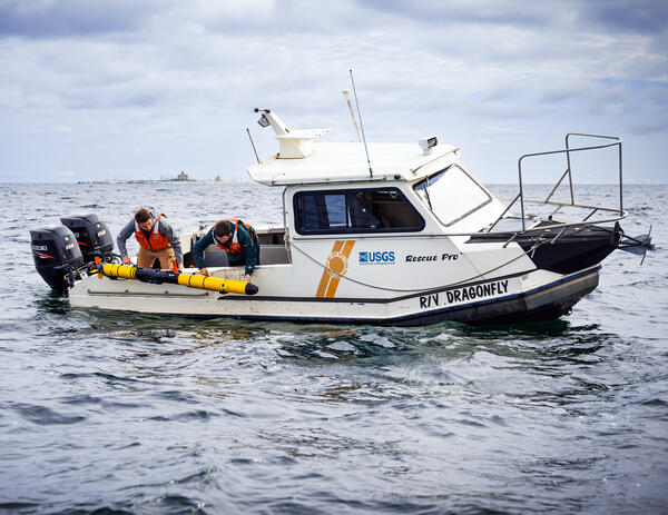 Two researchers on the R/V Dragonfly deploy a long yellow Autonomous Underwater Vehicle in Lake Michigan.