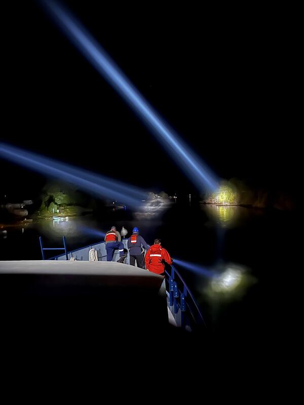 Crewmen on a research vessel use spotlights at night to aid navigation in a tight inlet