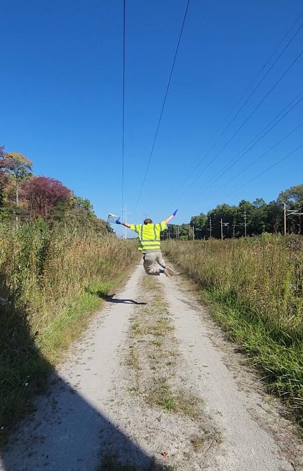 Man jumps as he walks away from the camera along a dirt trail