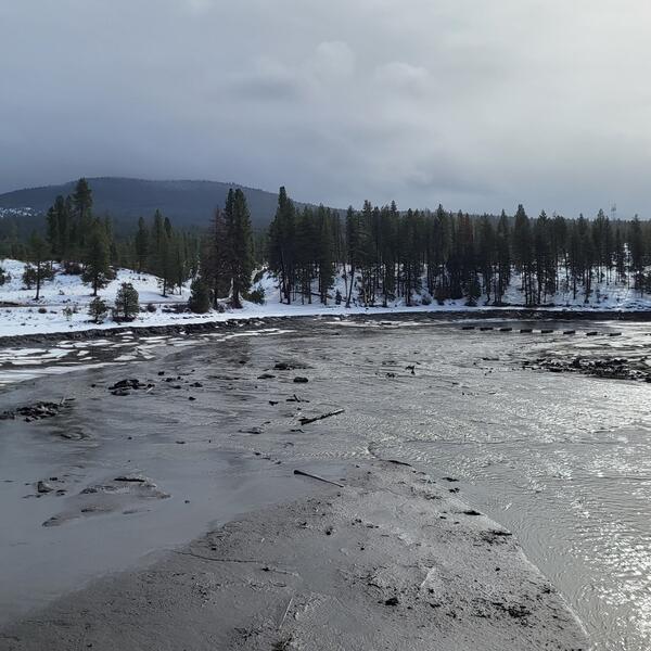 Klamath River flows through snow covered hills with sparse pine trees. Cloudy cold day