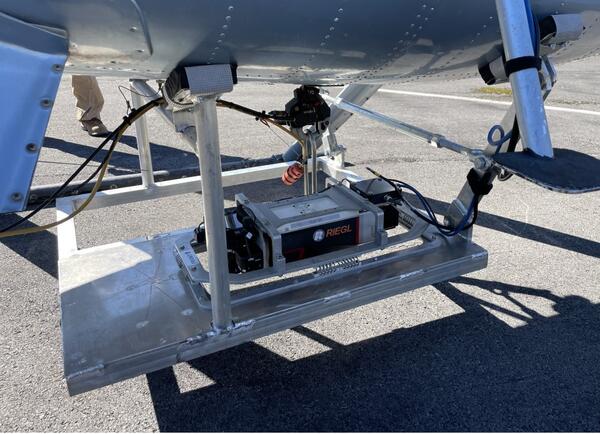Color photograph of instrument mounted to the bottom of a helicopter