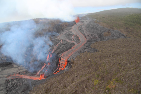 Molten glowing lava cascades over the rim of a crater after flowing through the jungle from an erupting fissure