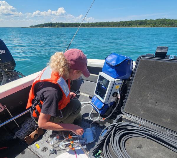 Researcher on a small vessel filtering water through an instrument on a sunny day.