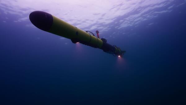 A view underwater in Lake Michigan looking up at a yellow Autonomous Underwater Vehicle with two lights shining down.