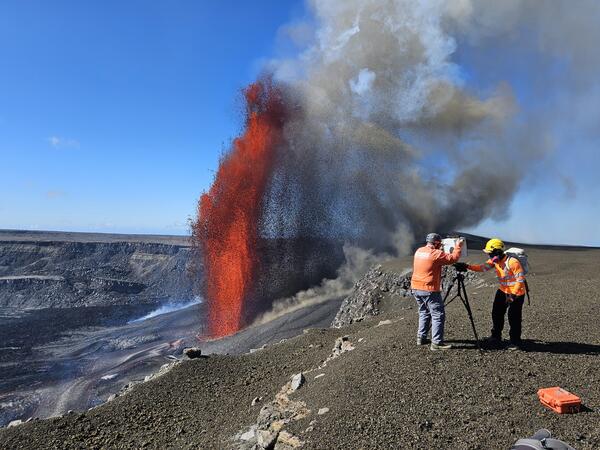 Color photograph of scientists setting up monitoring equipment next to lava fountain