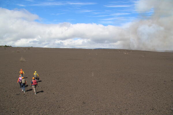 Color photograph of scientists walking across volcanic terrain to monitor eruption