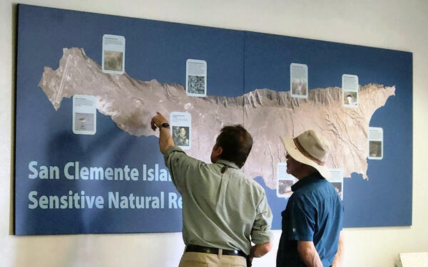 Scientist Charles Drost and Emeritus Mark Sogge look at a map of San Clemente Island on a wall