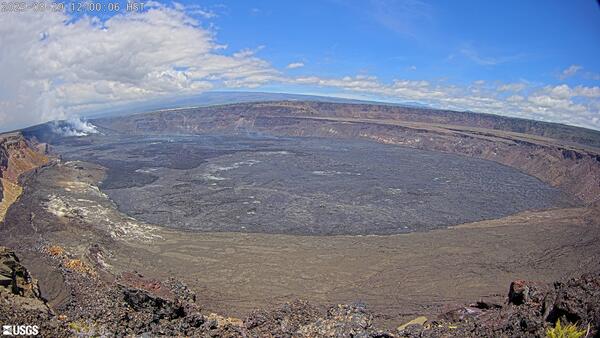 Desolate caldera with a steaming volcanic vent in the background under cloudy skies.