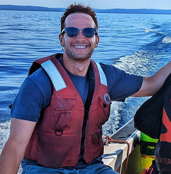 Researcher wearing a life vest sitting on a boat gunwale.